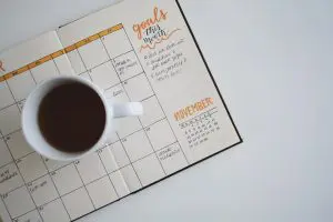 A coffee mug sits atop of an open monthly planner with notes.