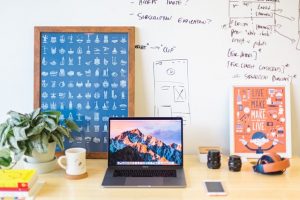 A desk space, featuring coffee mug, laptop and camera lenses. 